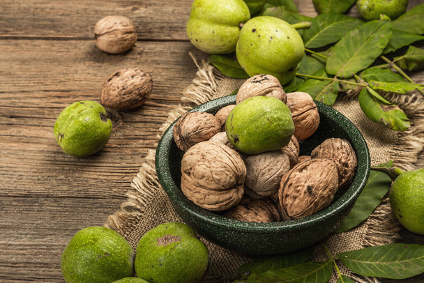 Ripe brown and unripe green walnuts in a bowl. Old wooden background, copy space - Foto, afbeelding