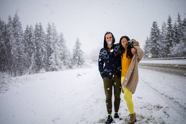 Winter Love Story. Mixed race couple walking in winter forest during a snowfall on holidays - Fotó, kép