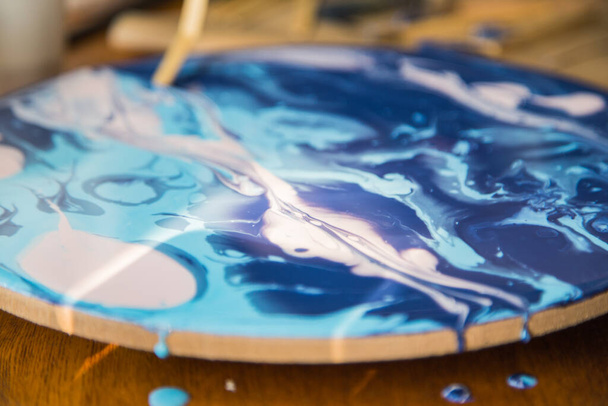 Female artist works on abstract fluid art painting with marble effect, close up portrait of beautiful young woman painter in process create art piece in creative workspace on a wooden table - Photo, image