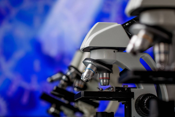 Крупный план микроскопа для различных масштабов увеличения или наблюдения, используемых в качестве аппарата в лаборатории микробиологии для исследования физических веществ и исследования клеток на синем фоне. - Фото, изображение