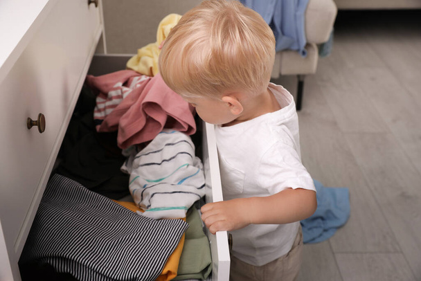 Cute little boy playing with clothes in dresser's drawer at home - Fotó, kép