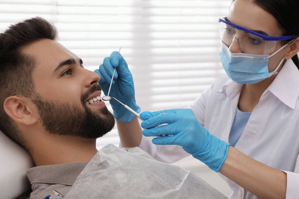 Dentist examining young man's teeth in modern clinic - Foto, Imagen