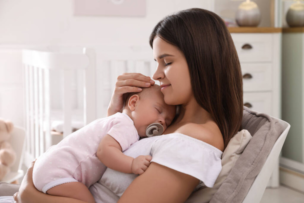 Happy young mother with her sleeping baby in armchair at home - Photo, Image