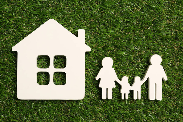 Family and house figures on green grass, flat lay - Foto, afbeelding