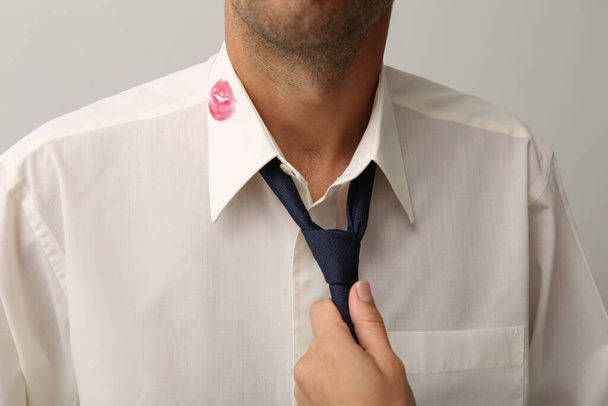 Woman grabbing her husband by tie due lipstick kiss mark on his shirt, closeup - Photo, image