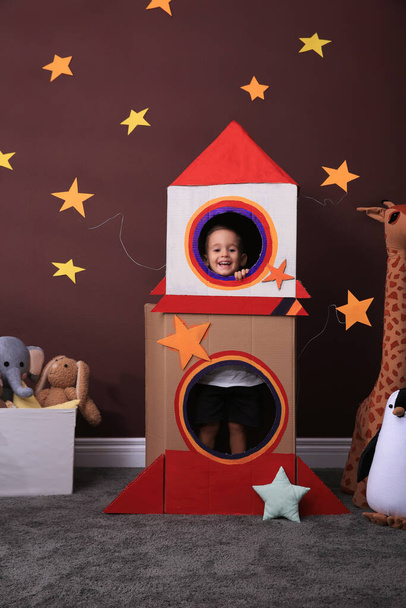 Cute little boy playing with cardboard rocket and toys at home. Child's room interior - Фото, зображення