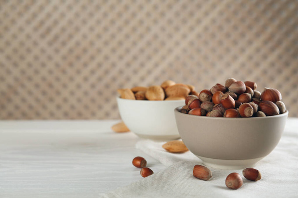 Ceramic bowl with hazelnuts on white wooden table, space for text. Cooking utensil - Photo, Image