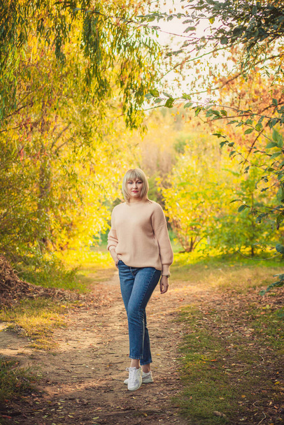 Une femme blonde avec une coupe de cheveux courte se promène dans la forêt dans un pull tricoté. Randonnées en plein air dans la forêt d'automne. - Photo, image