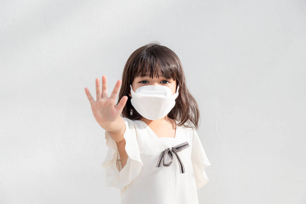 Возвращайся в школу. Маленькая азиатка в маске для защиты. Покажите стоп руки жест, чтобы остановить вспышку коронавируса. - Фото, изображение