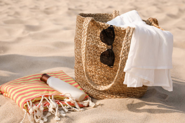 Beach bag, towel, blanket, sunglasses and sunscreen on sand - Foto, afbeelding