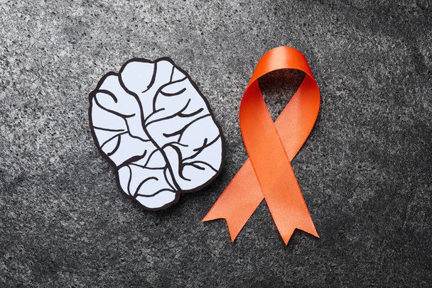 Orange ribbon and paper brain cutout on grey table, flat lay. Multiple sclerosis awareness - Fotó, kép