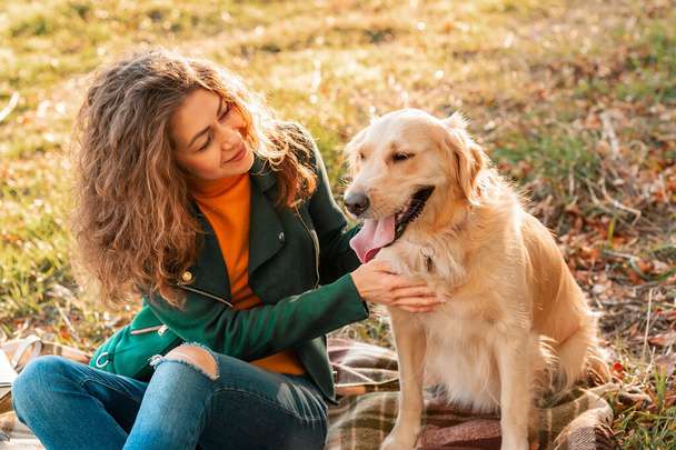 Young curly woman with her dog Golden retriever embracing outdoors - Photo, Image