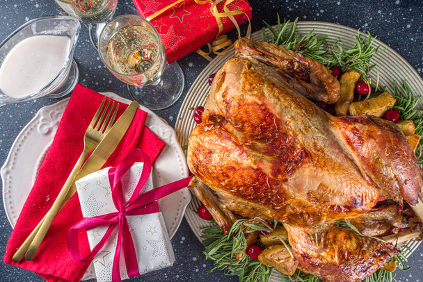 Christmas or New Year turkey dinner. Baked turkey with potato, red berries and sage leaves, on Christmas dinner table with Xmas tree, gift and candles background - Фото, изображение