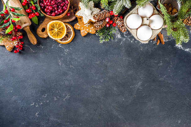 Ingredients for Christmas cooking, winter baking cookies, gingerbread, fruitcake, seasonal drinks. Cranberries, dried oranges, cinnamon, spices, flour on dark stone table, copy space top view - Fotó, kép