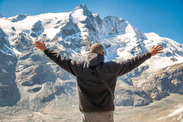 Ο άνθρωπος αγκαλιάζει τη φύση σε μια όμορφη καλοκαιρινή μέρα με χιονισμένα βουνά στο παρασκήνιο - Φωτογραφία, εικόνα
