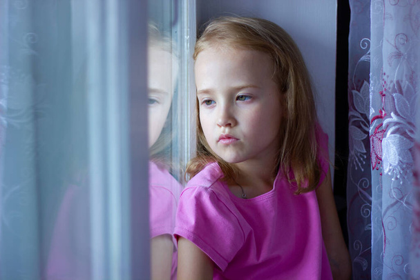 sad girl in a pink dress sits by the window, loneliness concept, isolation - Photo, Image