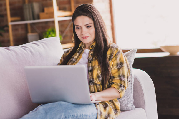 Photo of positive lady sit comfortable couch hold laptop typing surf social network wear plaid shirt home indoors - Photo, image