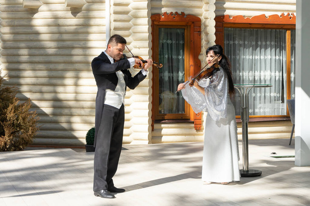 Dúo de violinistas. Un hombre con un frac y una mujer con un vestido de noche tocan el violín. - Foto, imagen
