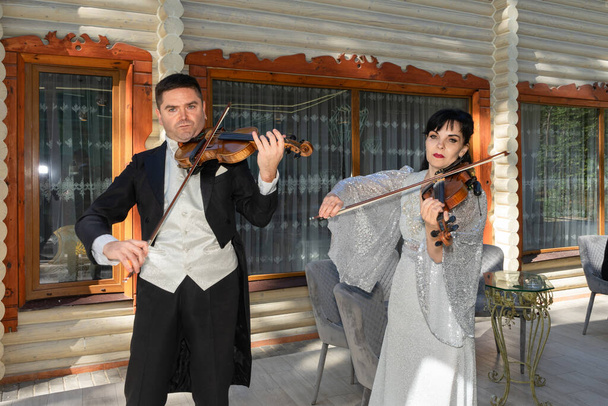 Duo de violonistes. Un homme en tailleur et une femme en robe de soirée jouent du violon. - Photo, image