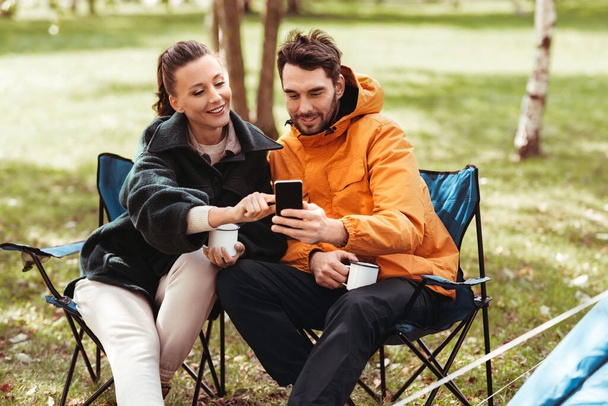 couple with smartphone drinking tea at campsite - Foto, Imagem