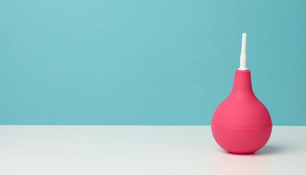 рожева гумова клізма на білому столі, медичний інструмент для очищення тіла, синій фон, копіювання простору
 - Фото, зображення