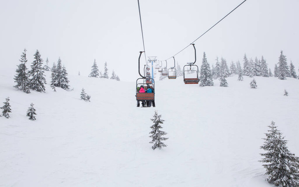 ski lift transports unrecognizable skiers over the snow-capped mountainside. cold winter cloudy day. winter active rest, sports hobbies, digital detox - Photo, image