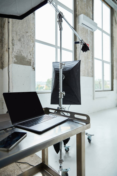 фотостудия с большими окнами, профессиональный фотосвет, стол, на котором ноутбук и телефон - Фото, изображение