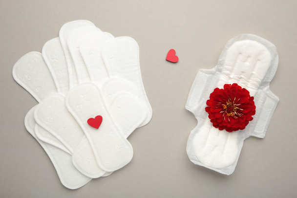 Menstrual pads on a grey background. A rose flower lies on a menstrual pad. Menstruation cycle. Hygiene and protection. Top view. - Photo, Image