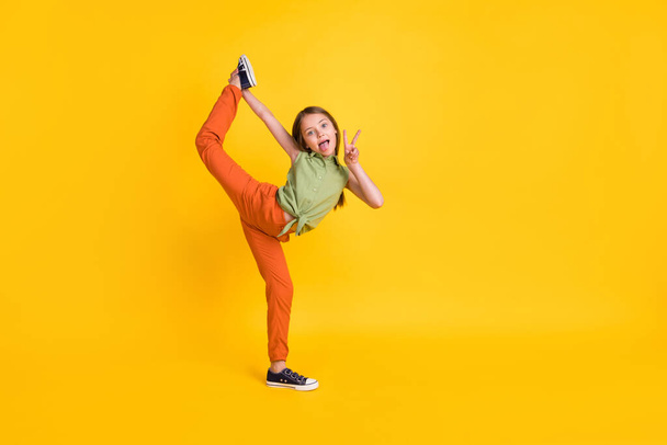Full length body size photo little girl showing v-sign doing stretching isolated vivid yellow color background - Zdjęcie, obraz
