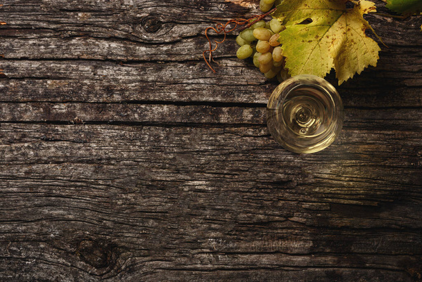 Bílé víno ve sklenici, hrozny a hroznové větve na stole. Horní pohled. Kopírovat mezeru pro text. - Fotografie, Obrázek