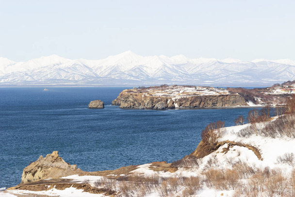 Paesaggio primaverile. Una baia con acqua azzurra, circondata da colline e rocce. Sullo sfondo si trovano vulcani e montagne innevate. Il concetto di vacanze invernali. - Foto, immagini