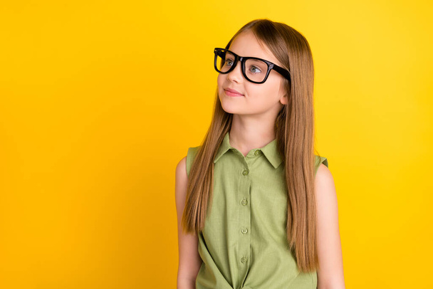 Photo of smart blond little girl look empty space wear spectacles khaki blouse isolated on yellow color background - Foto, immagini