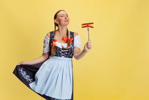 Comic portrait of beautiful Oktoberfest woman, waitress wearing a traditional Bavarian or german dirndl isolated on yellow studio background. - Фото, зображення
