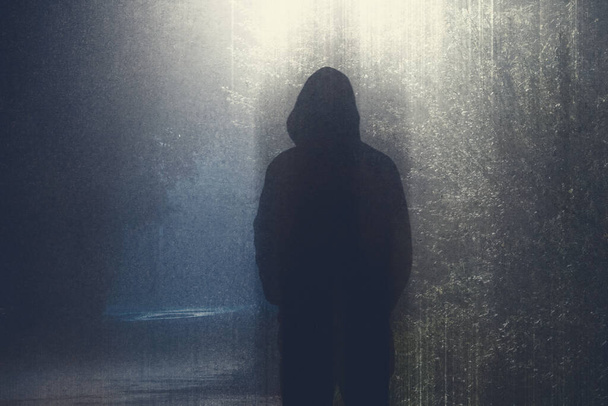 A hooded figure silhouetted against a street light lighting up a country road. On a foggy night. With a grunge edit - Photo, Image