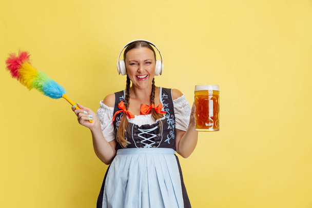Komisches Porträt der schönen Wiesn-Frau, Kellnerin im traditionellen bayerischen oder deutschen Dirndl isoliert auf gelbem Studiohintergrund. - Foto, Bild