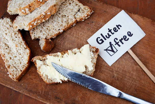 Un pedazo de pan sin gluten con mantequilla en una tabla de madera. Signo sin gluten. - Foto, Imagen