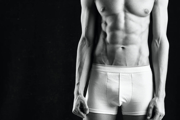 αρσενικό αθλητή σε λευκό σορτς φουσκωμένο σώμα bodybuilder το σκούρο φόντο - Φωτογραφία, εικόνα