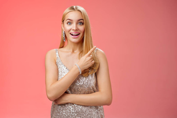 Joyful surprised good-looking blond woman talking friend during party smiling broadly look camera amused wondered pointing upper right corner curious discuss awesome room design, red background - Foto, Bild