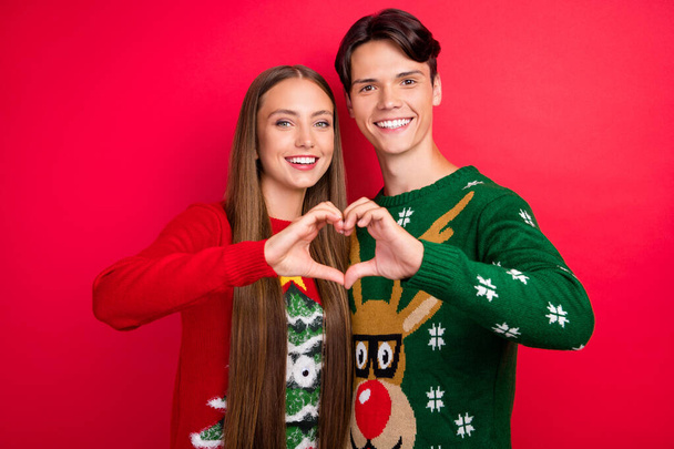 Photo of cheerful two lovers fingers demonstrate heart figure wear ugly sweater isolated red color background - Foto, immagini