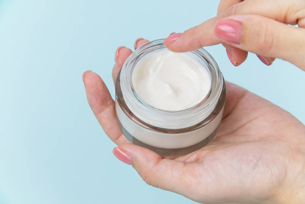 Health and beauty theme female hand holding a glass jar with white body care cream on background. - Photo, Image