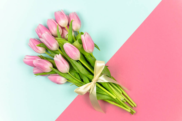 Un ramo de tulipanes rosados atados con una cinta sobre un fondo azul y rosa. Flores de primavera. Día Internacional de la Mujer. Día de San Valentín. Concepto de Pascua. Vista superior - Foto, imagen