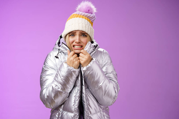 Uncomfortable shaking displeased charming gloomy blond cute woman in silver stylish jacket pulling coat tight wear hat shaking clenching teeth grimacing suffering low temperature freezing cold - Фото, изображение