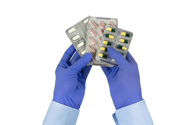 Packs van pillen in artsen handen geïsoleerd op witte achtergrond Mannelijke handen in blauwe latex handschoenen. - Foto, afbeelding
