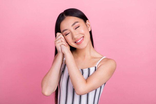 Photo of sweet dreamy young lady wear striped outfit arms cheek closed eyes smiling isolated pink color background - Zdjęcie, obraz