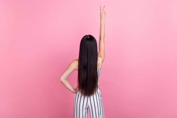 Photo of slim funny young lady wear striped outfit standing back showing v-sign isolated pink color background - Fotoğraf, Görsel