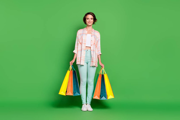 Full body photo of cheerful happy positive woman smile hold hands shopping bags isolated on green color background - Foto, immagini