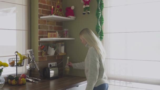 Een jonge mooie blonde komt in de keuken en corrigeert objecten en diverse decoraties. Kerstmis - Video