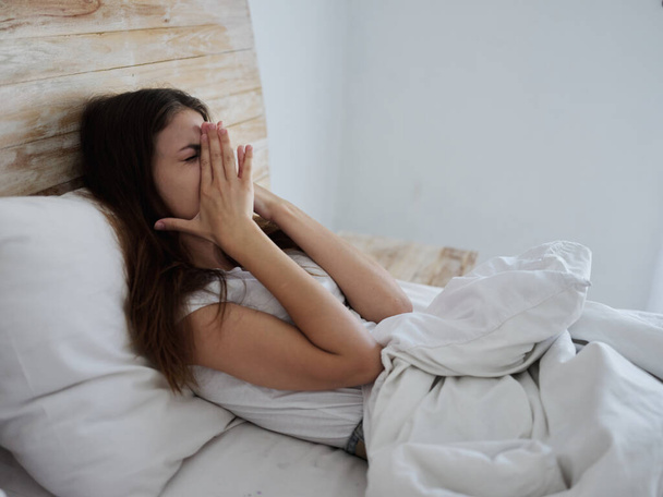 femme avec un rhume se trouve dans le lit mains sur le visage émotions problèmes de santé - Photo, image