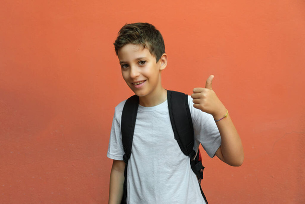 Elementary schoolboy with thumb up isolated against an orange wall. back to school concept. - 写真・画像