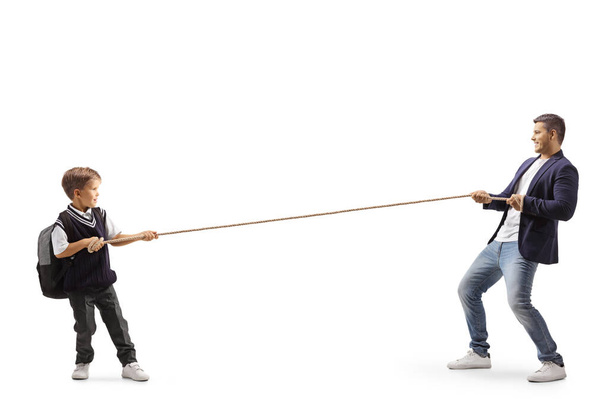 Full length profile shot of a little schoolboy and a young man pulling a rope isolated on white background - Foto, Imagen